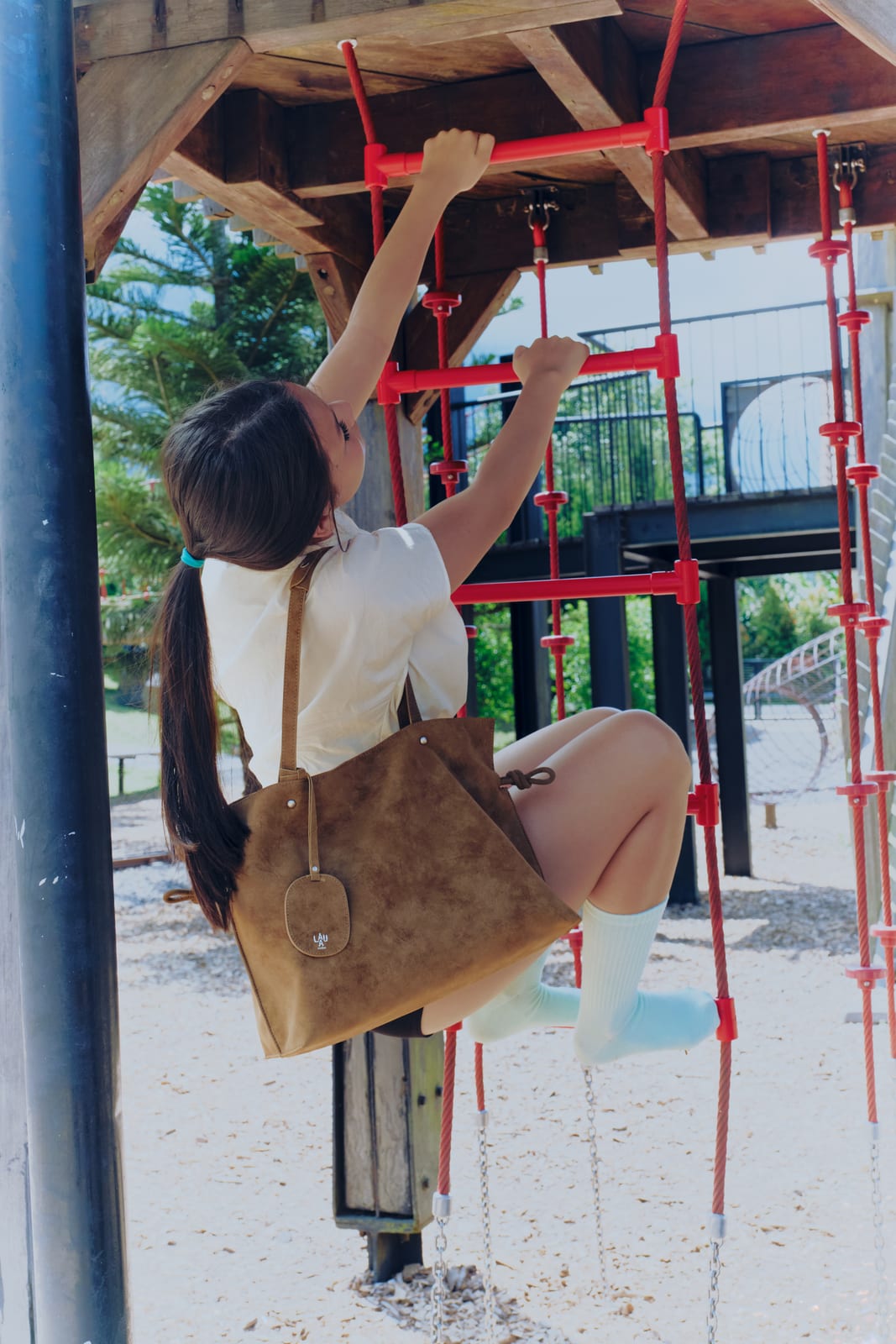 Isabelle Bag in Earth — under a red climbing frame at the playground
