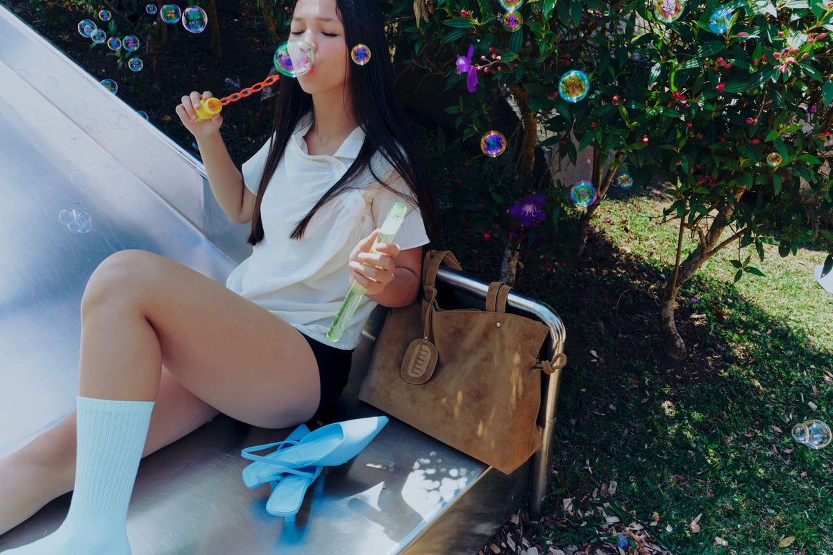 Isabelle Bag in Earth — campaign, blowing bubbles on a slide