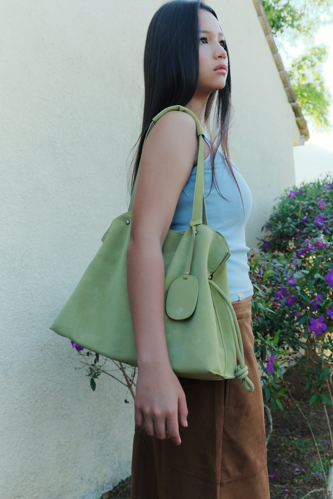 Isabelle Bag in Meadow — campaign, on the shoulder by a garden wall
