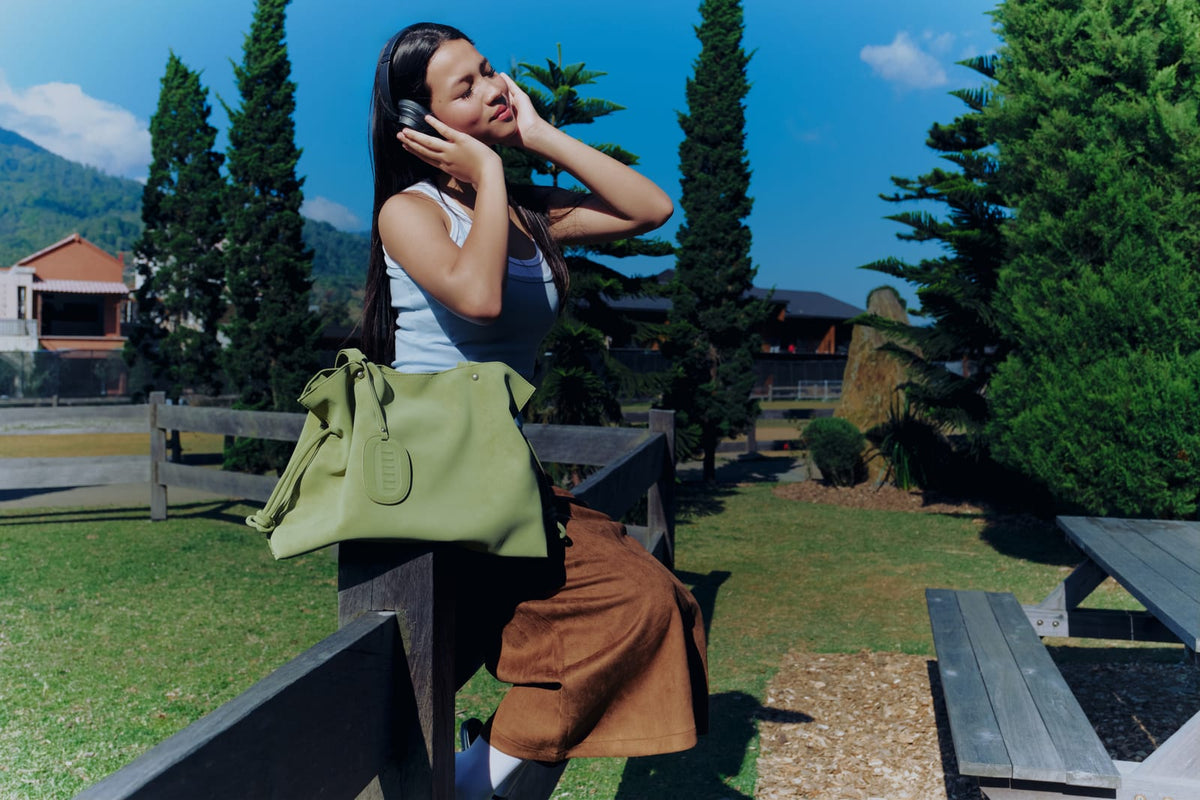 Isabelle Bag in Meadow — campaign, on a fence under blue sky