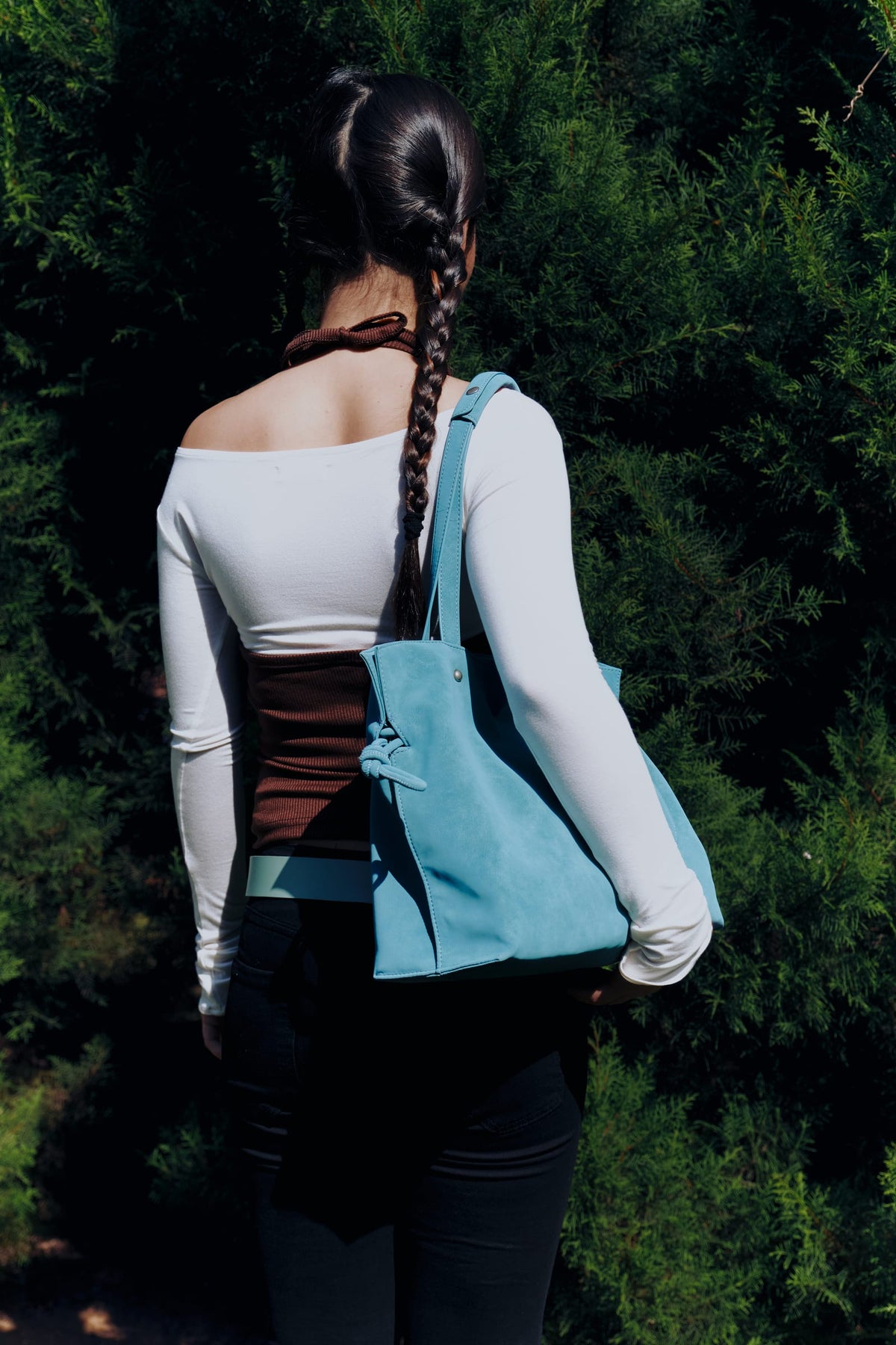 Isabelle Bag in Sky — campaign, worn on the shoulder from behind against a green hedge